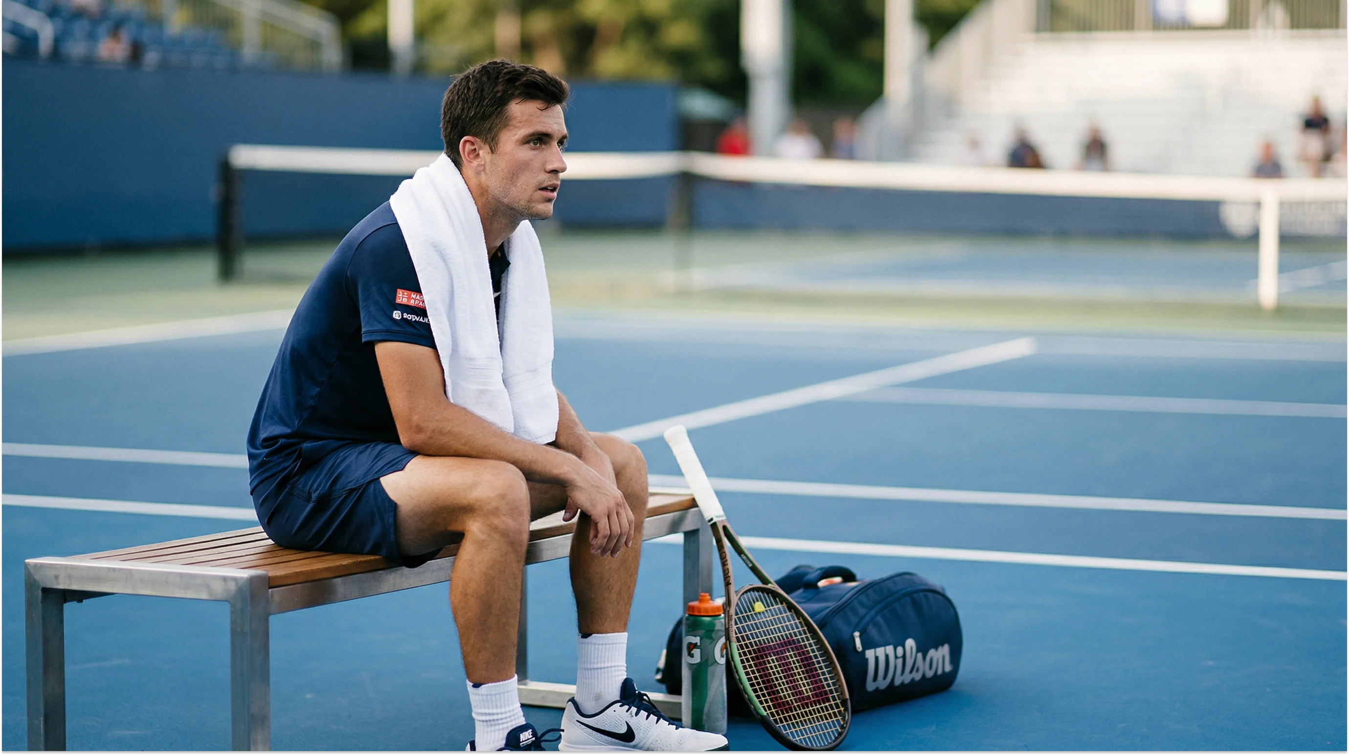 Tennisspieler sitzt beim Seitenwechsel auf der Bank und blickt konzentriert auf den Platz